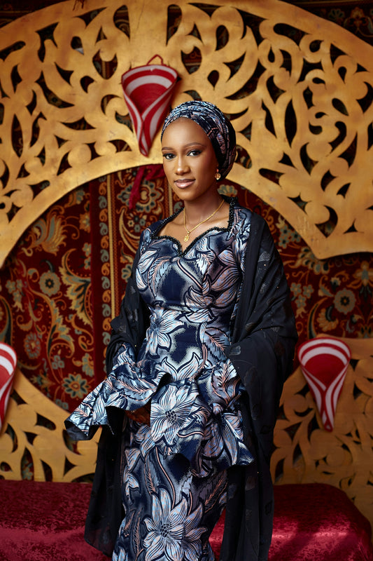 Elegant woman in patterned traditional dress against an ornate backdrop.